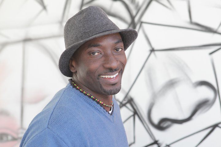Mahomed Bamba sorrindo, de chapéu e suéter azul